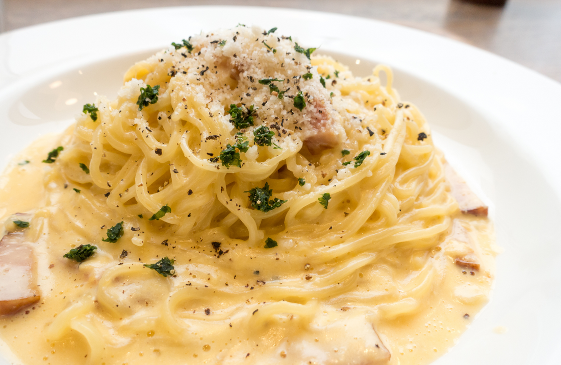 Close up of a shallow white bowl filled with linguine and creamy sauce, garnished with cheese and herbs.