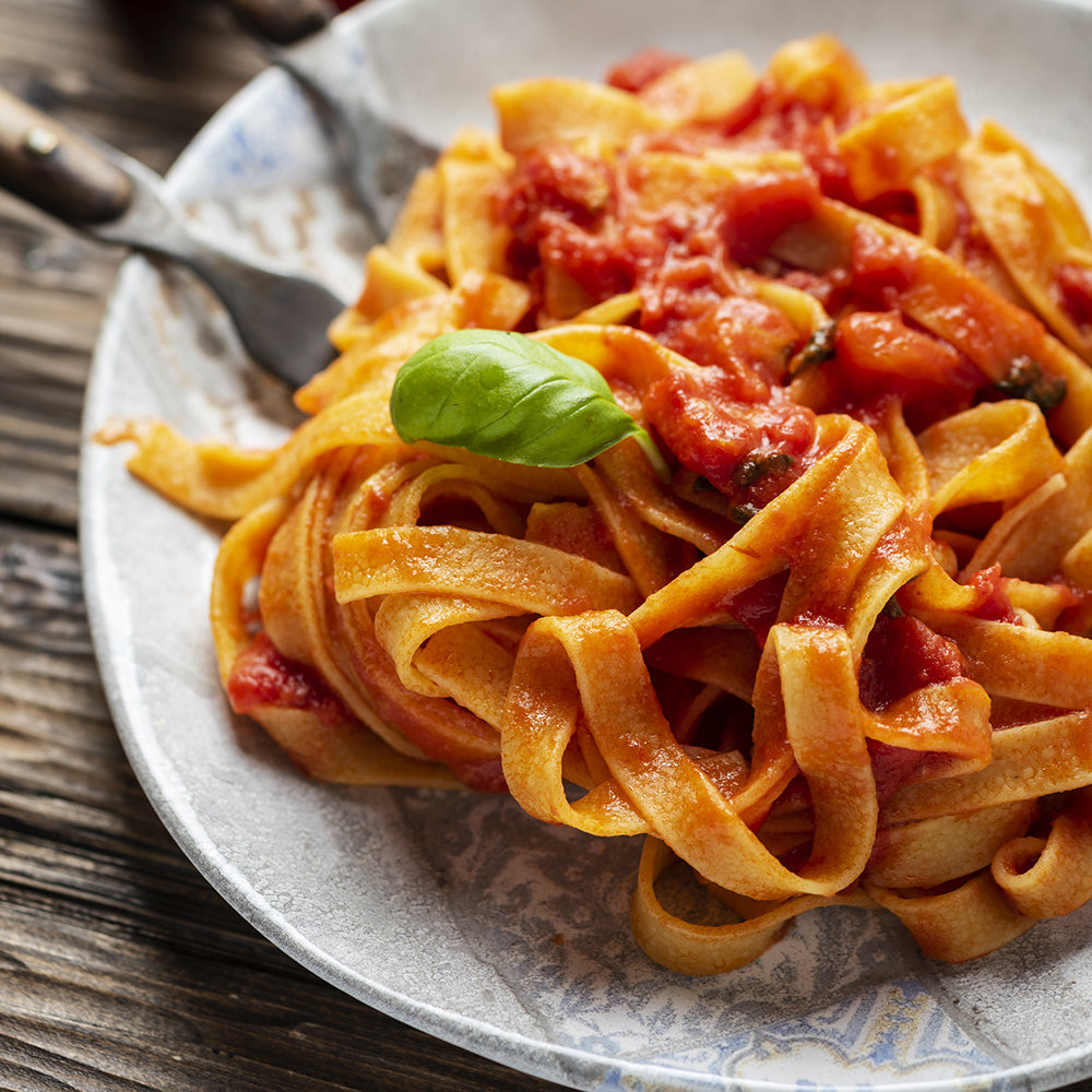 Close up of cooked Dagostino fettuccine coated with Dagostino Spicy Tomato Sauce and garnished with fresh basil.