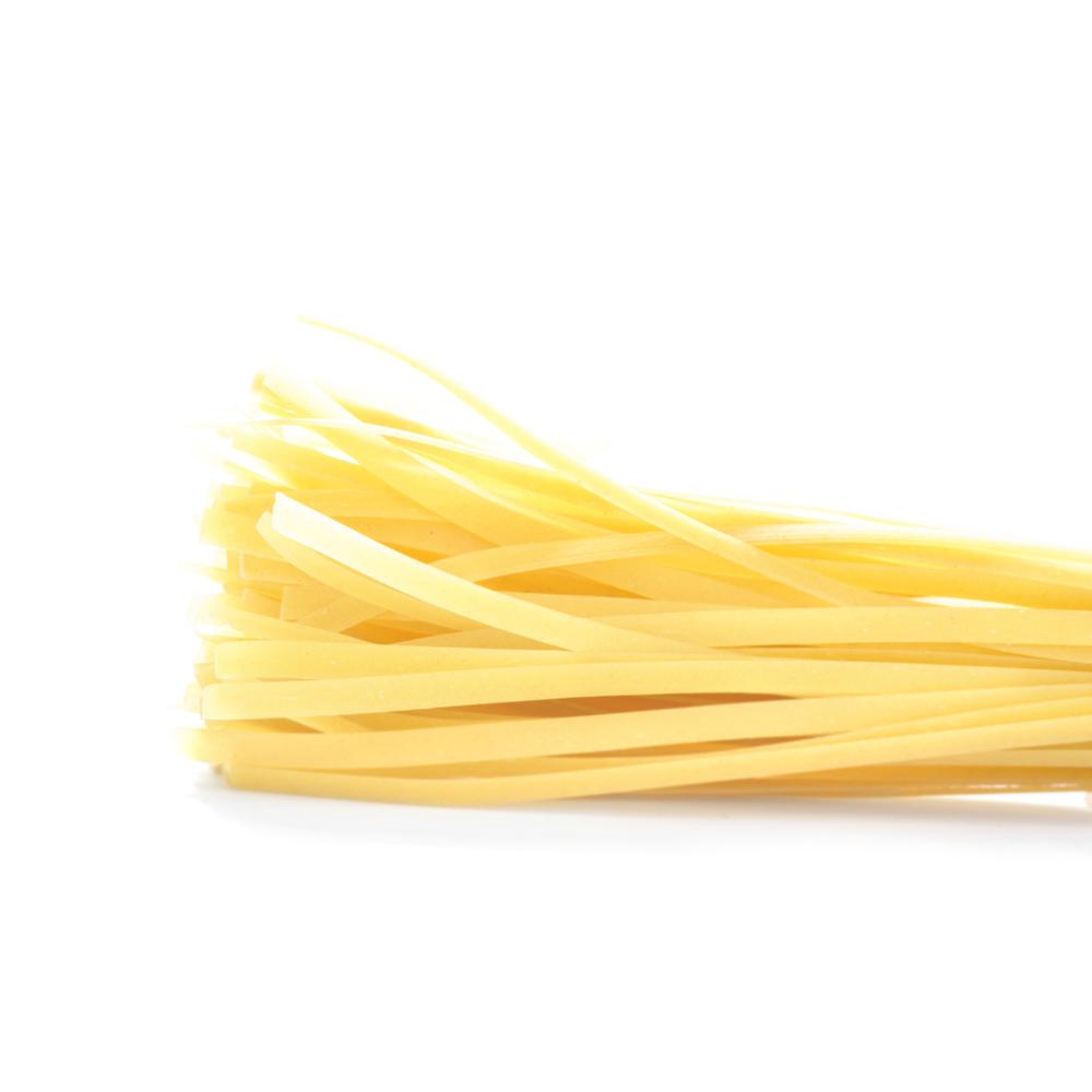 Close up of the thick, flat, yellow strands of dried Dagostino Fettuccine Pasta against a white background.
