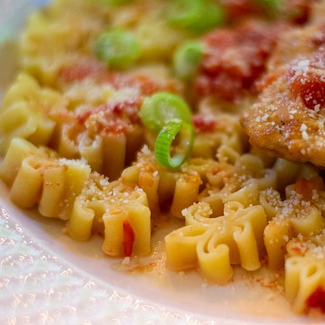 Close up of a plateful of Fleur de Lis Pasta with Pomodoro Sauce, garnished with green onions and grated cheese.