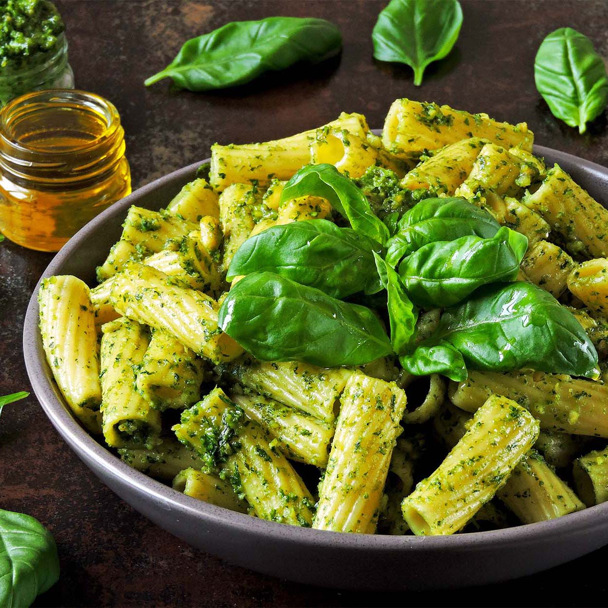 Close up of a gray bowl filled with penne rigate pasta and pesto sauce garnished with fresh basil leaves