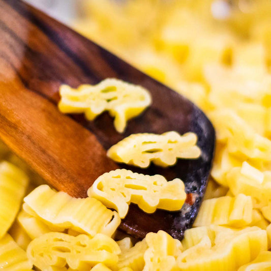 Close up of several pieces of cooked alligator shaped pasta on a wooden spoon