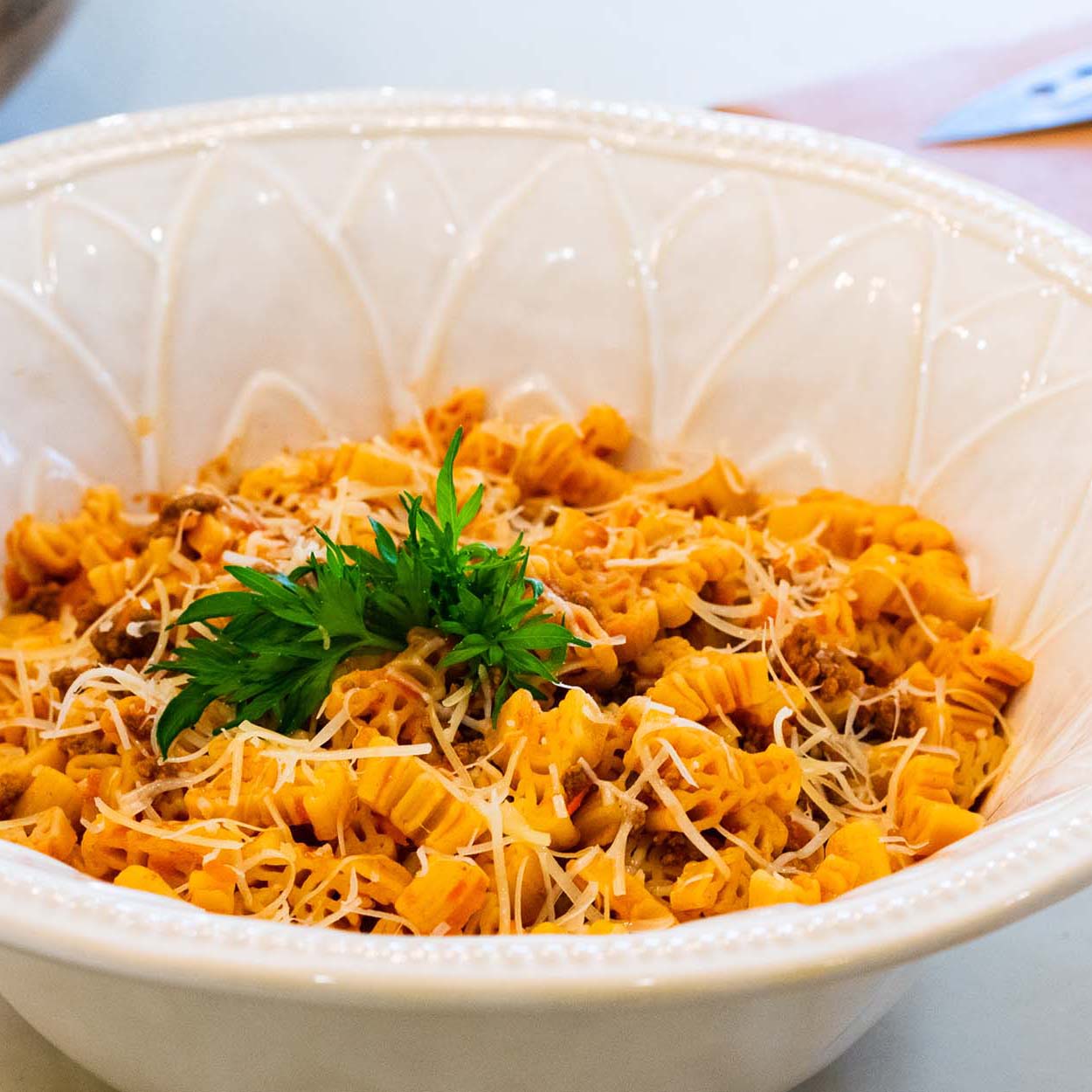 Close up of a white bowl filled with crawfish shaped pasta in a light red sauce, garnished with cheese and fresh herbs.